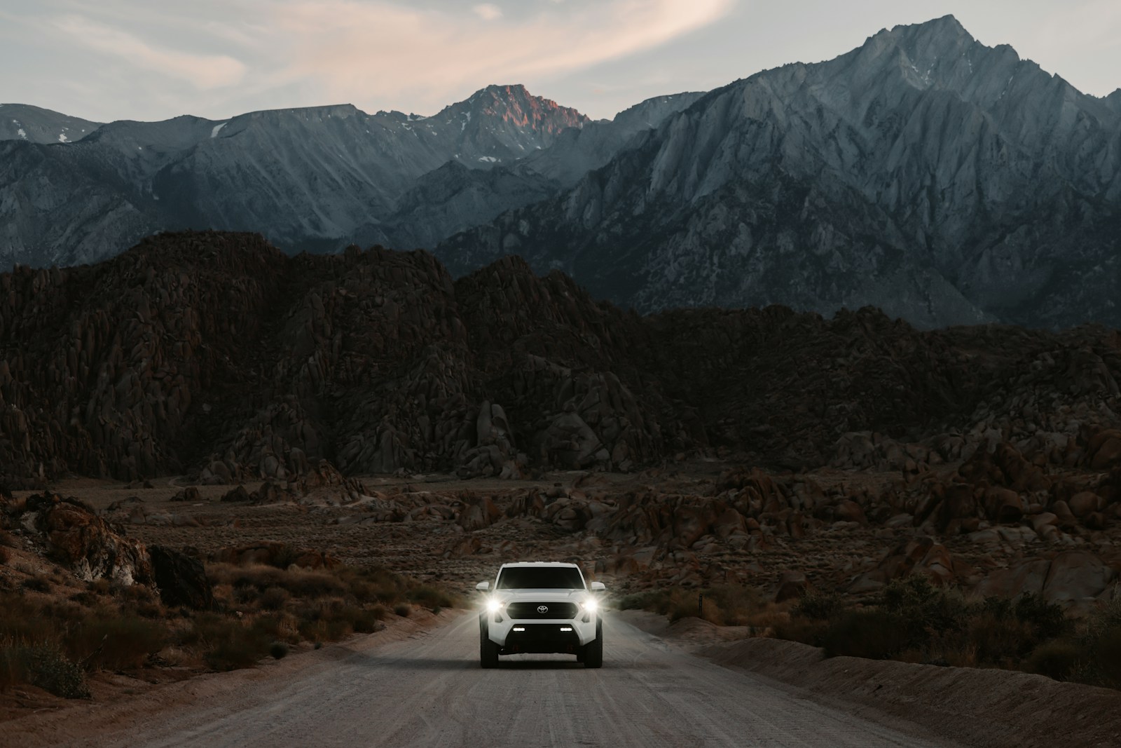 White truck drives on a dirt road towards mountains